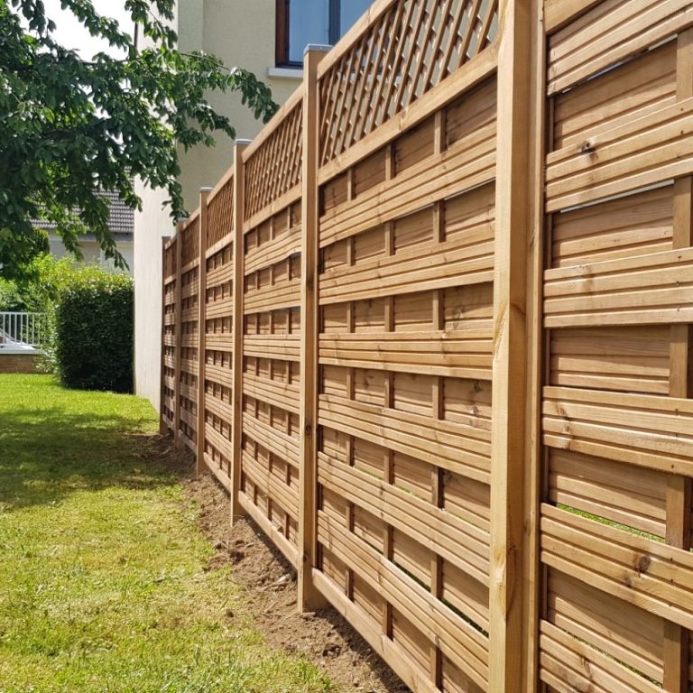 Clôture en bois avec motifs, entourant un jardin verdoyant.